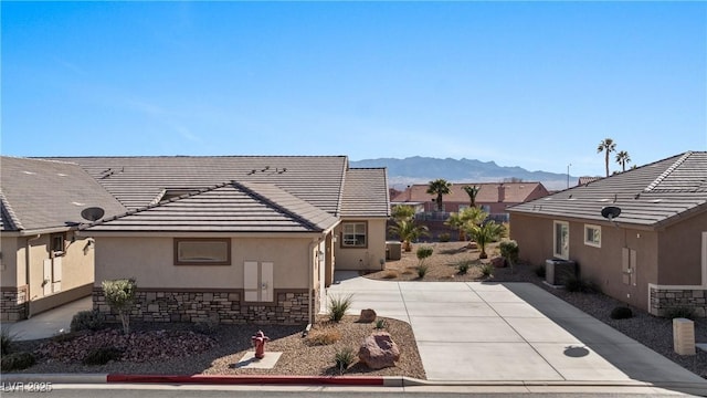 view of side of property with a tile roof, stucco siding, driveway, stone siding, and a mountain view