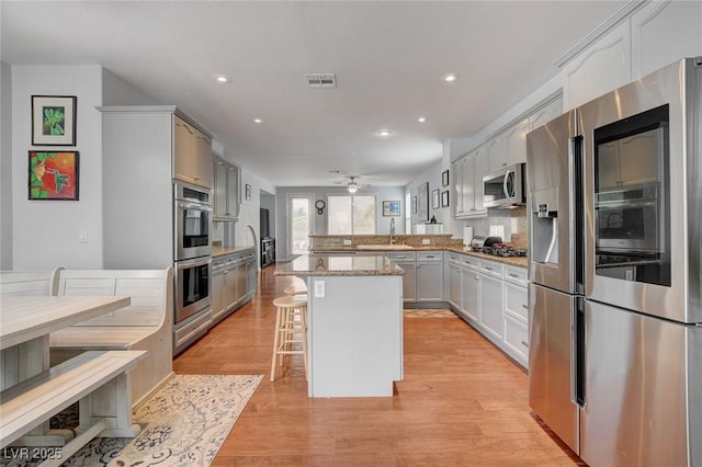 kitchen featuring visible vents, ceiling fan, a peninsula, light wood-style floors, and stainless steel appliances