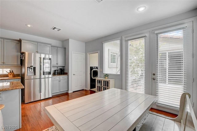 kitchen with visible vents, gray cabinetry, light wood-style flooring, light stone counters, and stainless steel fridge