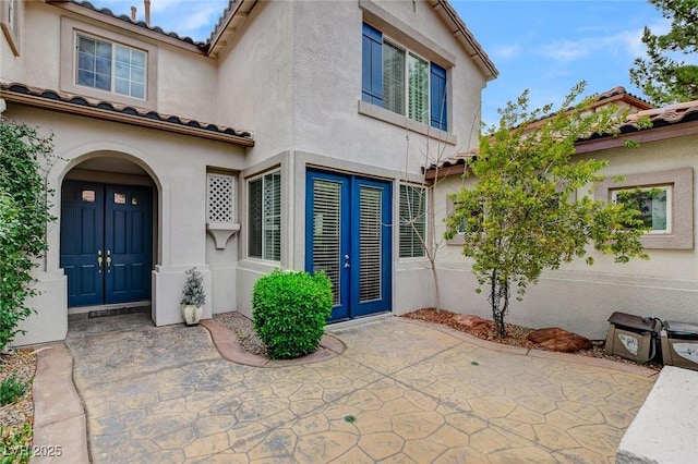 view of exterior entry featuring stucco siding, a tiled roof, and french doors