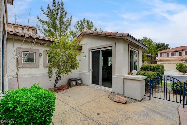 back of property with stucco siding, a tile roof, and a gate