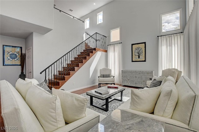 living area featuring stairway, wood finished floors, visible vents, baseboards, and a towering ceiling