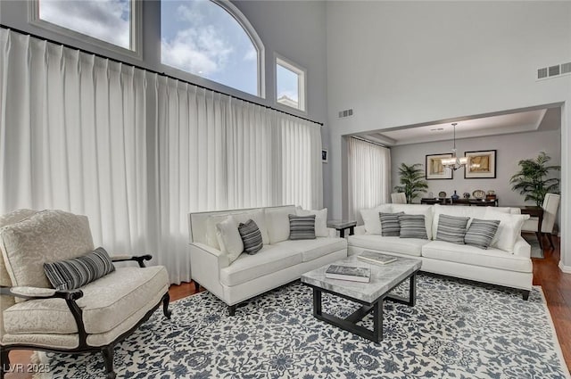 living area with an inviting chandelier, a high ceiling, wood finished floors, and visible vents