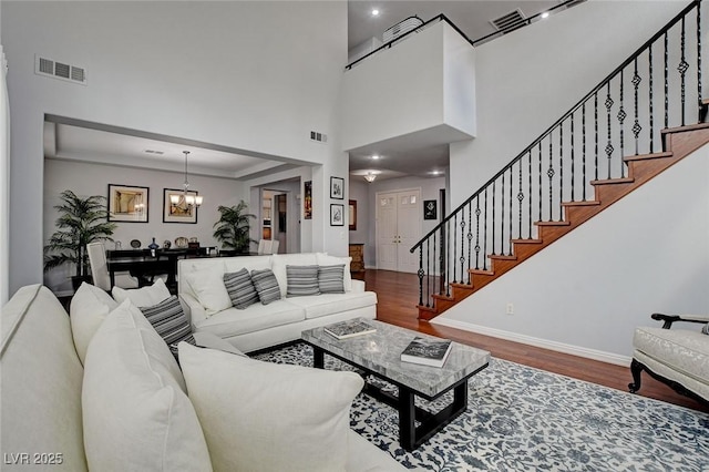 living room with a chandelier, visible vents, stairs, and wood finished floors