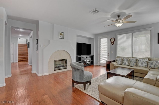 living room featuring wood finished floors, visible vents, a ceiling fan, a fireplace, and stairs