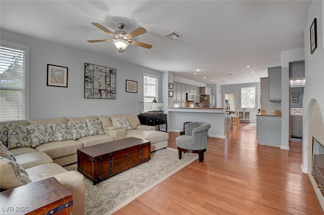 living room featuring a ceiling fan, visible vents, a wealth of natural light, and light wood-type flooring