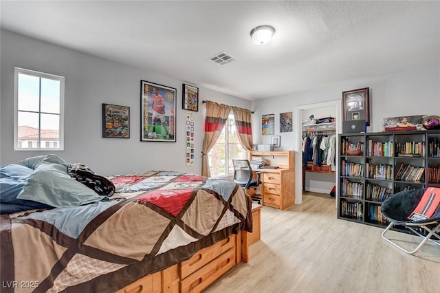 bedroom featuring a closet, visible vents, a walk in closet, and light wood-style floors