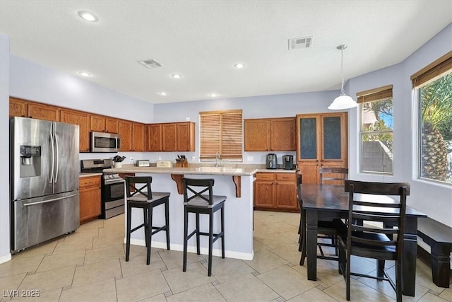 kitchen with visible vents, a breakfast bar area, light countertops, appliances with stainless steel finishes, and brown cabinetry