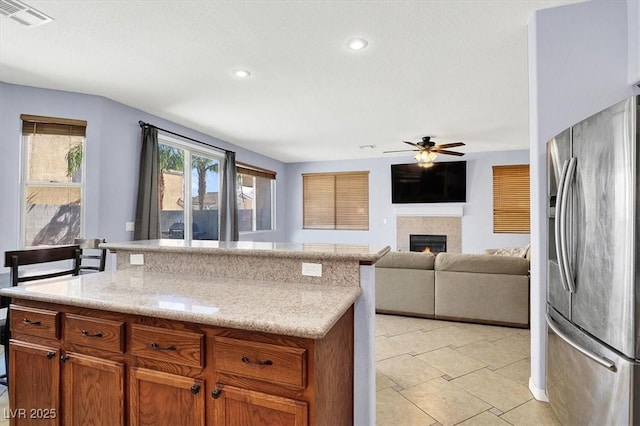 kitchen with visible vents, a ceiling fan, a lit fireplace, brown cabinetry, and stainless steel fridge with ice dispenser