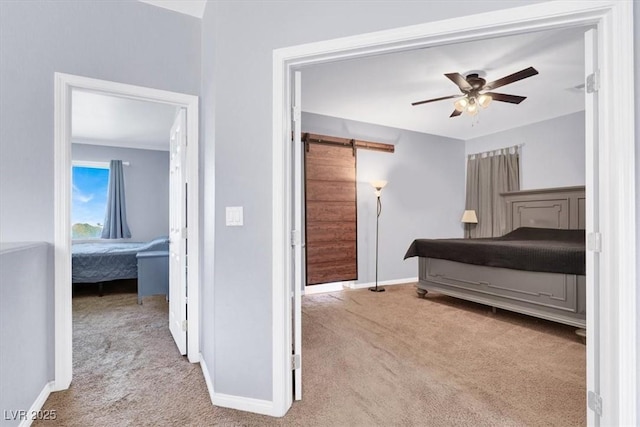 carpeted bedroom with a barn door, baseboards, and a ceiling fan