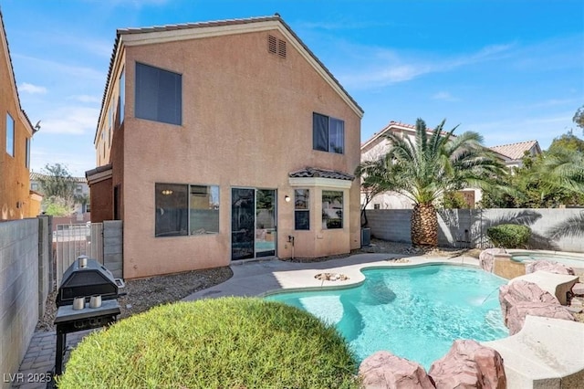 rear view of property featuring stucco siding, a pool with connected hot tub, a fenced backyard, and a tiled roof