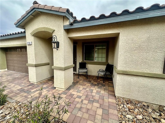 doorway to property with stucco siding, a patio, an attached garage, and a tile roof