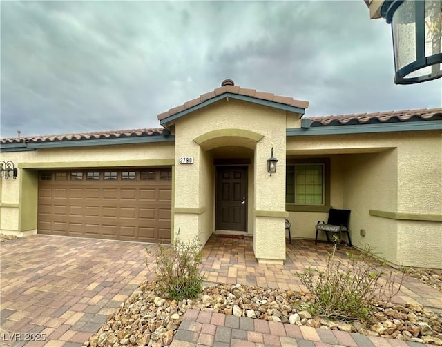 entrance to property with a tiled roof, decorative driveway, a garage, and stucco siding