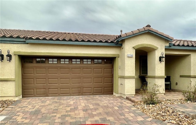 mediterranean / spanish home with stucco siding, driveway, an attached garage, and a tiled roof