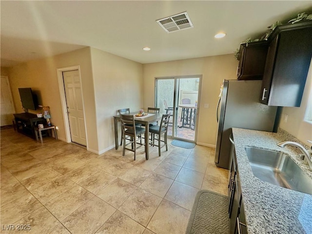 kitchen featuring visible vents, baseboards, light stone counters, recessed lighting, and a sink