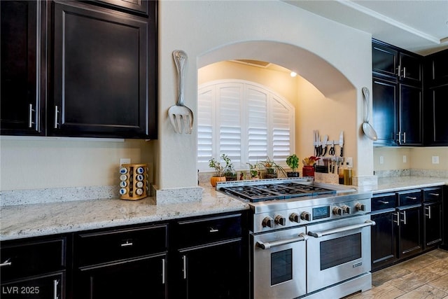 kitchen with light wood-style flooring, double oven range, light stone countertops, and dark cabinets