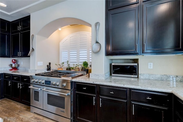 kitchen with stainless steel appliances, light stone countertops, light wood-style floors, and dark cabinetry