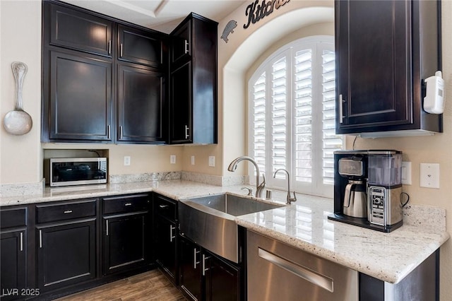 kitchen with a sink, stainless steel appliances, light stone countertops, and wood finished floors