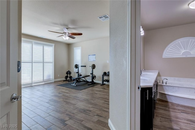 exercise room with visible vents, baseboards, ceiling fan, wood finished floors, and a sink