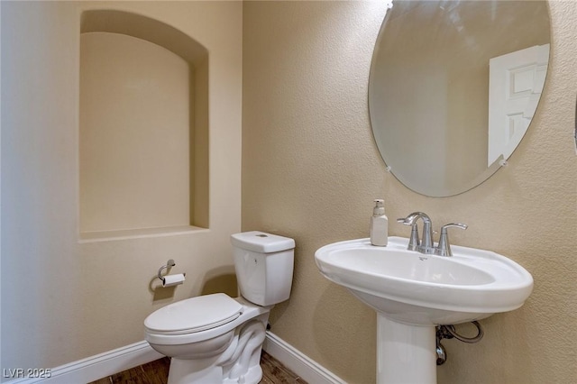 half bath with a textured wall, toilet, baseboards, and wood finished floors