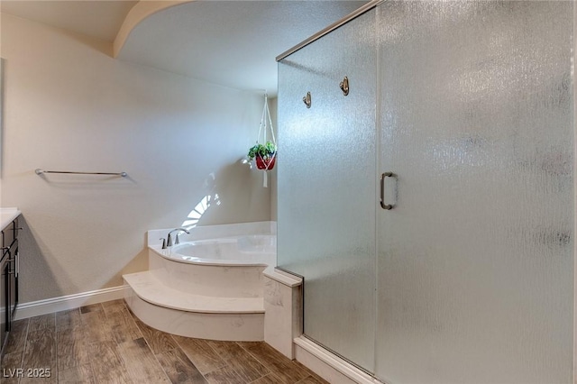 full bathroom featuring baseboards, a stall shower, wood finished floors, a bath, and vanity