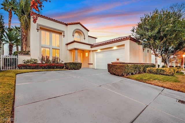 mediterranean / spanish-style home featuring stucco siding, driveway, fence, an attached garage, and a tiled roof