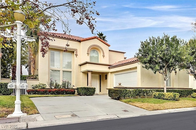 mediterranean / spanish-style home with a tiled roof, an attached garage, driveway, and stucco siding