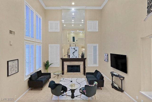 living room featuring a high ceiling, a glass covered fireplace, crown molding, and tile patterned flooring