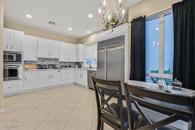 kitchen with a wealth of natural light, visible vents, backsplash, light countertops, and built in appliances