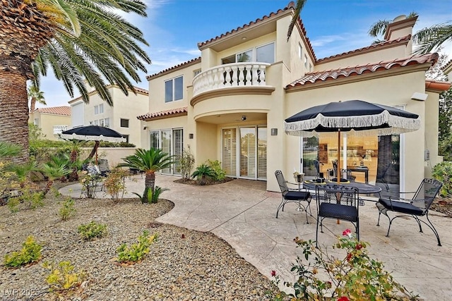 rear view of house featuring a tiled roof, stucco siding, a balcony, and a patio area