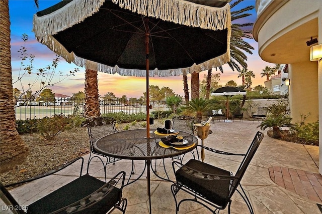 patio terrace at dusk featuring outdoor dining area and fence