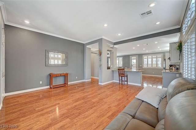 living room featuring light wood-type flooring, visible vents, baseboards, and ornamental molding