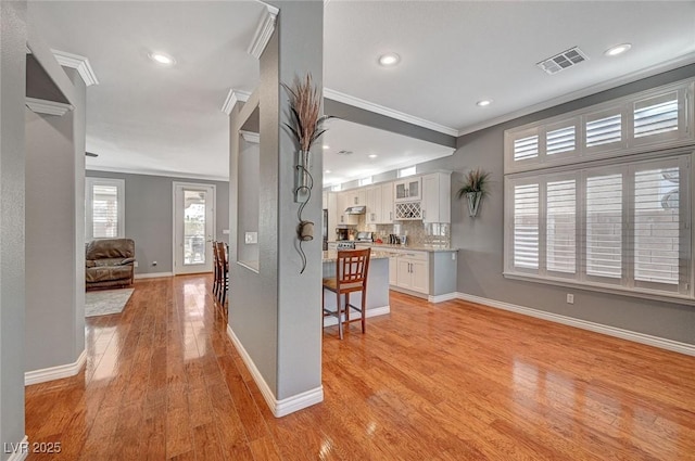 kitchen featuring visible vents, light wood-type flooring, a breakfast bar, crown molding, and open floor plan