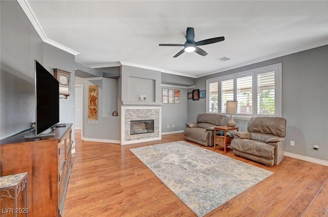 living area featuring ceiling fan, a glass covered fireplace, visible vents, and light wood-type flooring