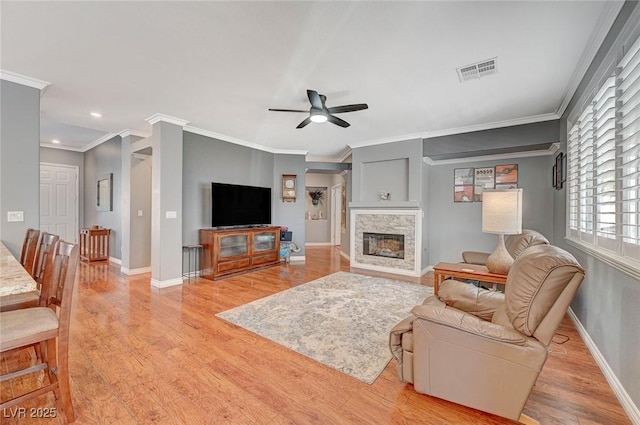 living area featuring a fireplace, light wood-style flooring, a ceiling fan, and visible vents