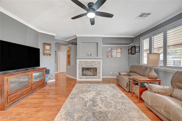 living room with visible vents, baseboards, ceiling fan, light wood-style flooring, and a glass covered fireplace