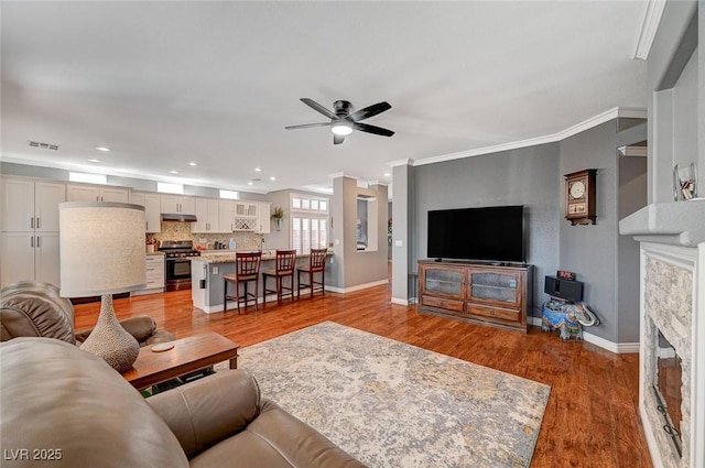 living room featuring baseboards, visible vents, ceiling fan, crown molding, and light wood-type flooring