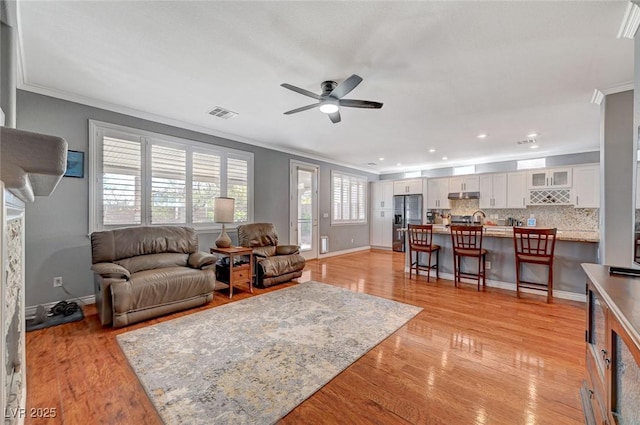 living area with visible vents, crown molding, light wood-style floors, and ceiling fan