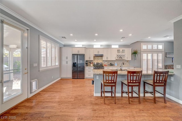 kitchen featuring a kitchen bar, under cabinet range hood, white cabinetry, appliances with stainless steel finishes, and light wood finished floors