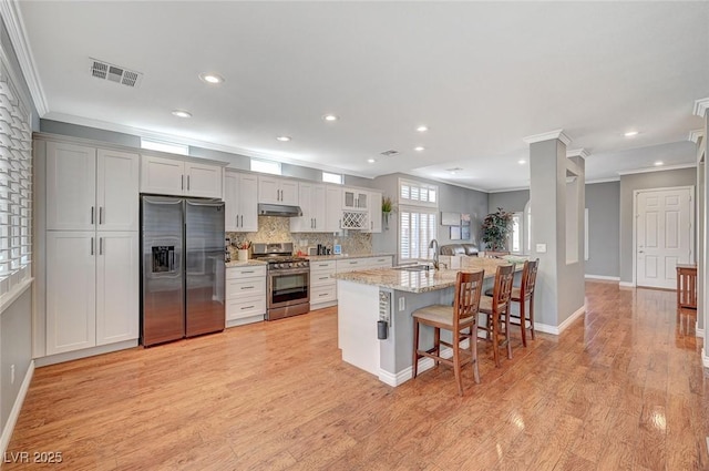 kitchen with visible vents, light wood finished floors, a sink, stainless steel appliances, and a kitchen bar