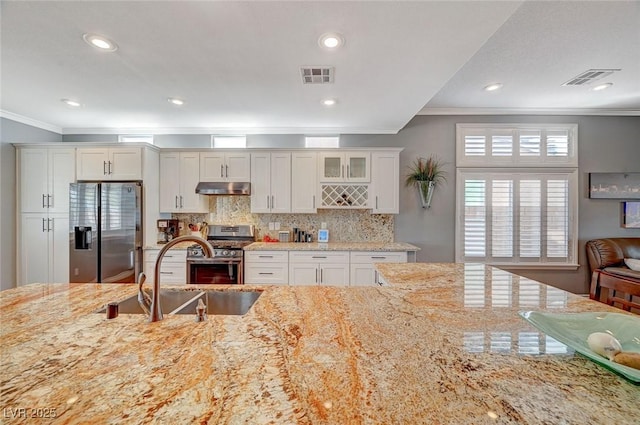 kitchen featuring visible vents, crown molding, under cabinet range hood, appliances with stainless steel finishes, and a sink