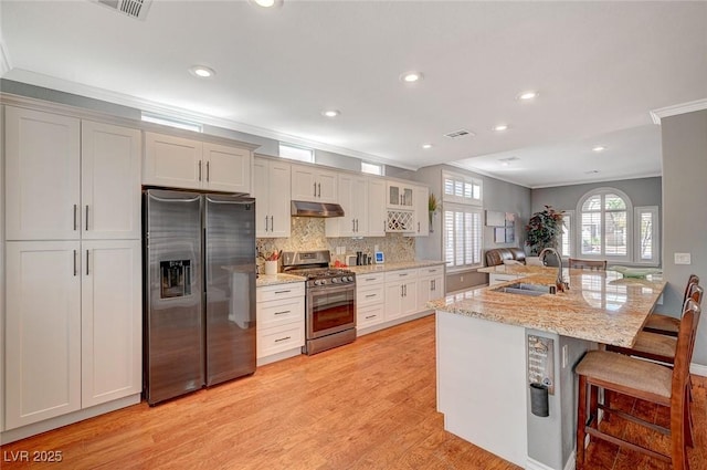 kitchen with ornamental molding, a sink, under cabinet range hood, appliances with stainless steel finishes, and a kitchen breakfast bar