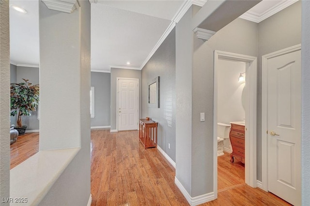 hall featuring baseboards, crown molding, and light wood-style floors