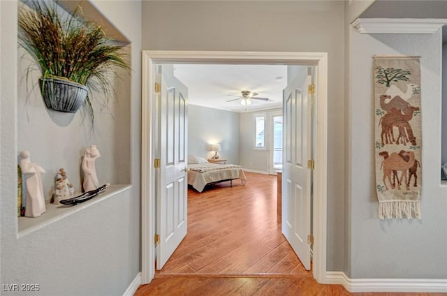 hall featuring light wood-style flooring and baseboards