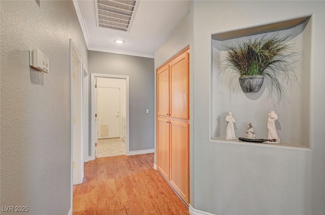 corridor featuring light wood-type flooring, visible vents, baseboards, and ornamental molding