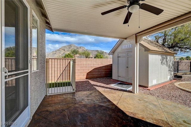 view of patio with a storage unit, an outbuilding, ceiling fan, and fence