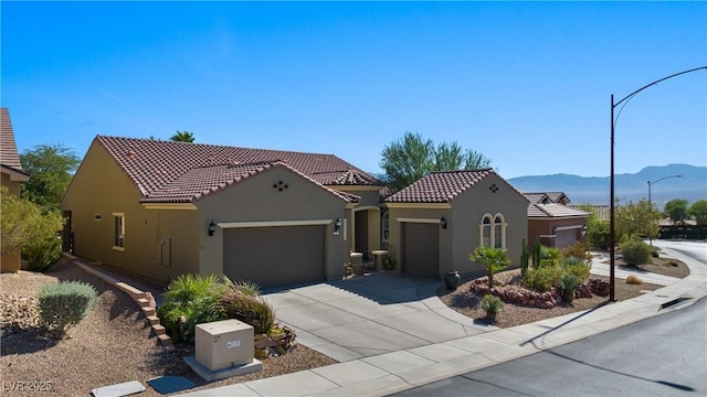 mediterranean / spanish-style house with a tiled roof, a mountain view, stucco siding, and an attached garage