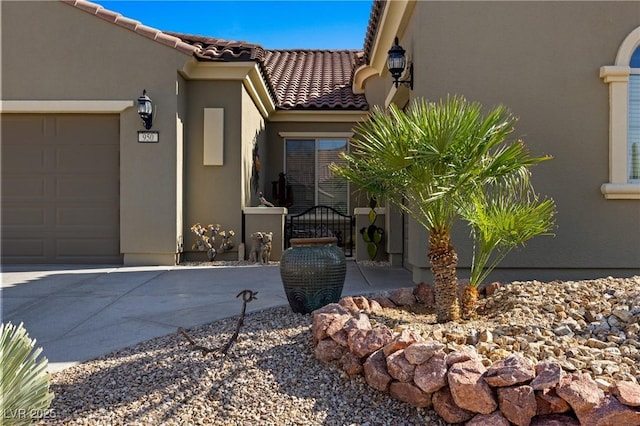 entrance to property with a tiled roof, a garage, driveway, and stucco siding