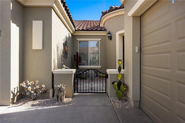 view of exterior entry featuring stucco siding, a tiled roof, a garage, and a gate