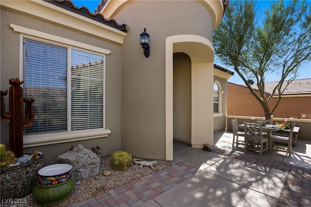 doorway to property with a tiled roof, stucco siding, outdoor dining area, and a patio area